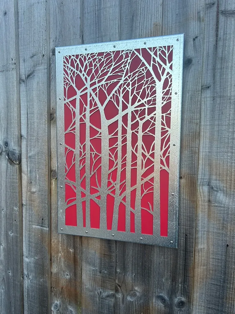 Silver laser-cut forest screen with bright red backing plate on a wooden fence
