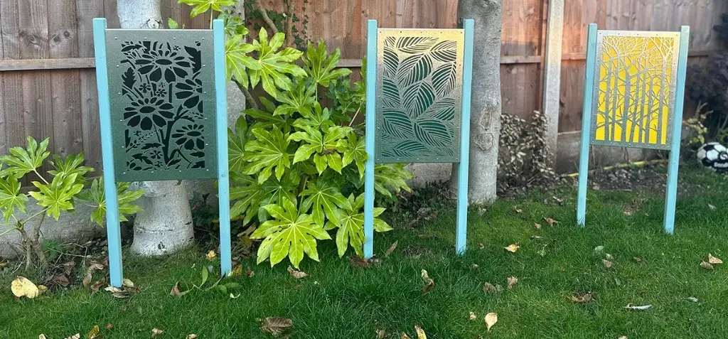 Three bespoke laser-cut garden screens installed between posts in a residential garden