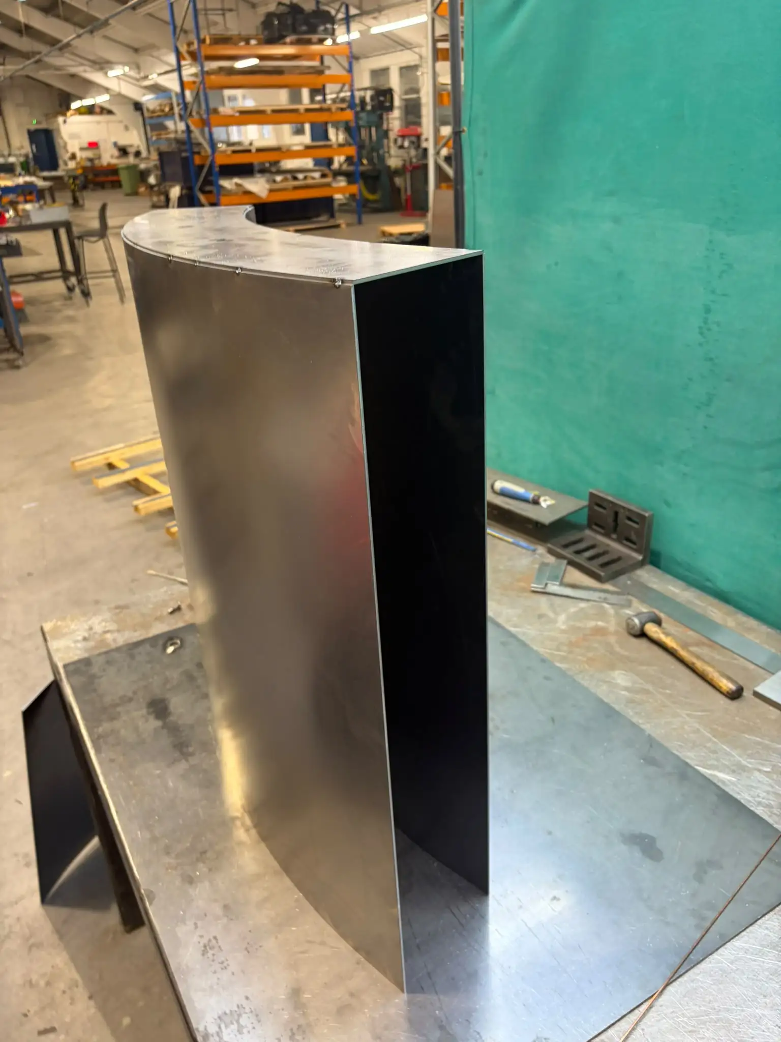 Dining table base upright with a curved face and dark side panel standing on the welding table