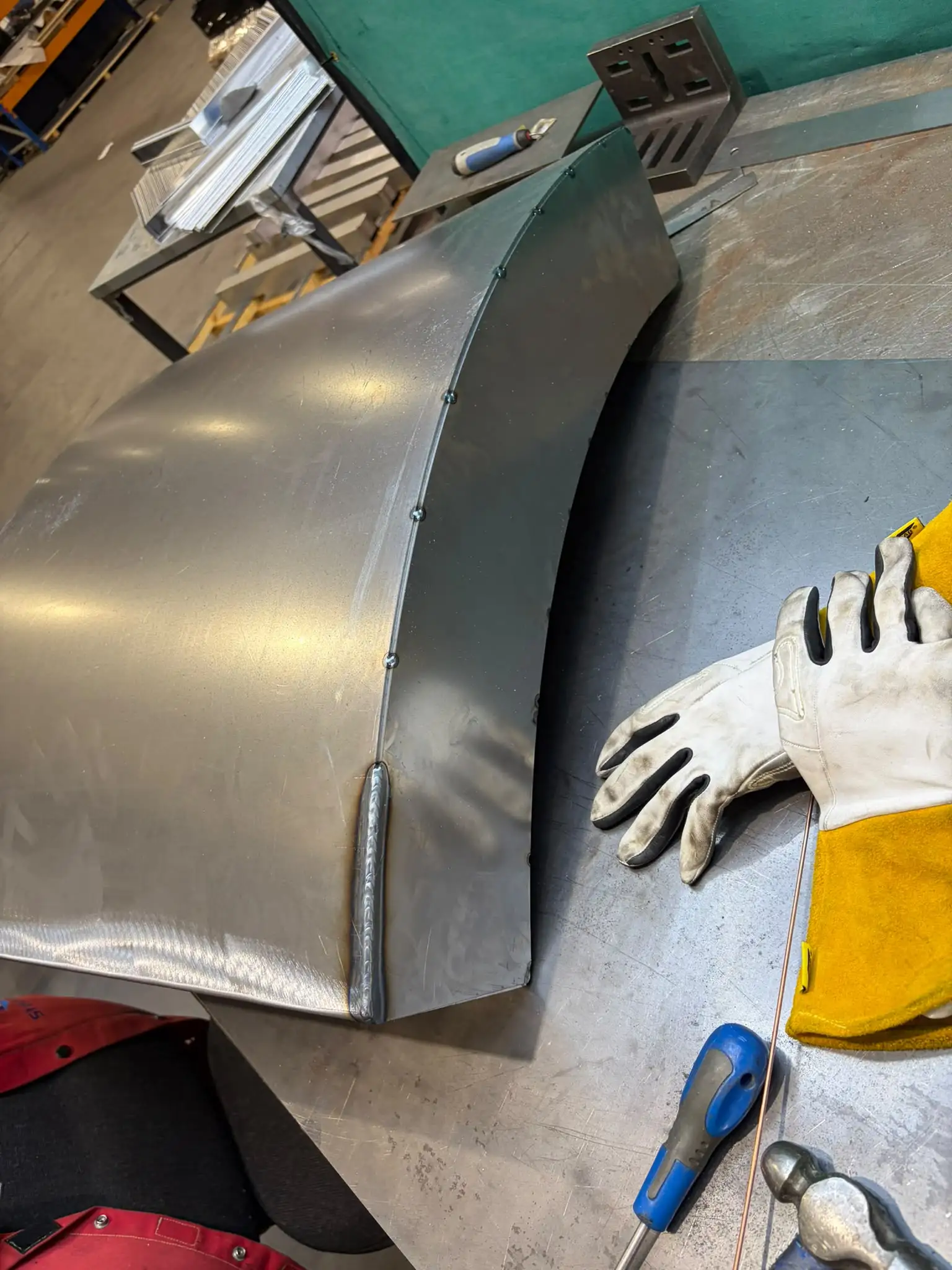 Curved base shell on the bench showing tack welds along the edge and a welded corner seam