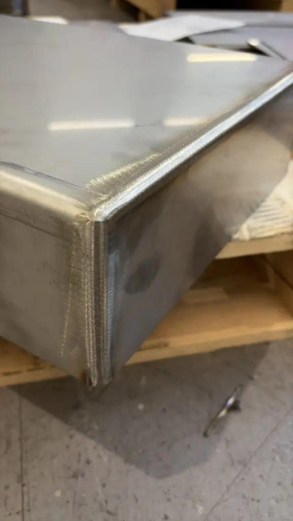 Close-up of a dressed and brushed corner weld on a stainless industrial magnet case