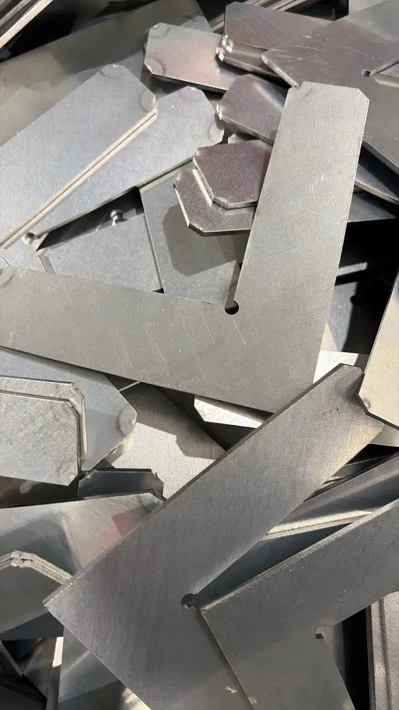 Pile of identical laser-cut L-shaped industrial shims with chamfered corners and a locating notch at the inner angle
