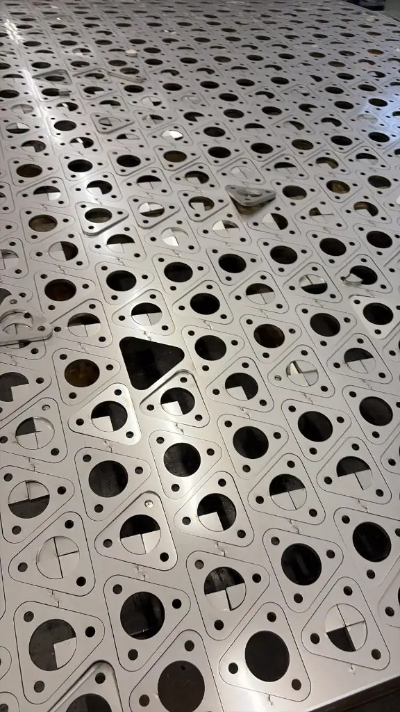 Full sheet of laser-cut triangular parts, each with a large centre hole and three smaller holes, nested for a production run