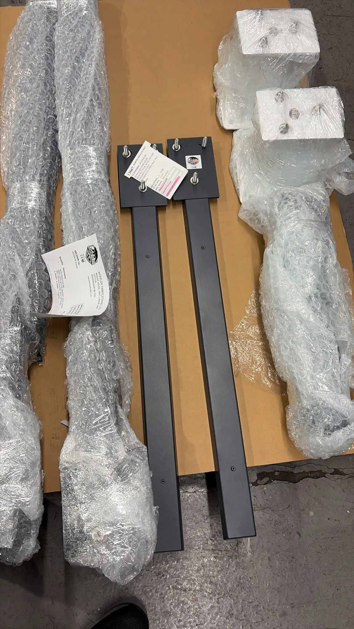 Dark grey Load Bear brackets with stud plates, bubble-wrapped companions and packing labels