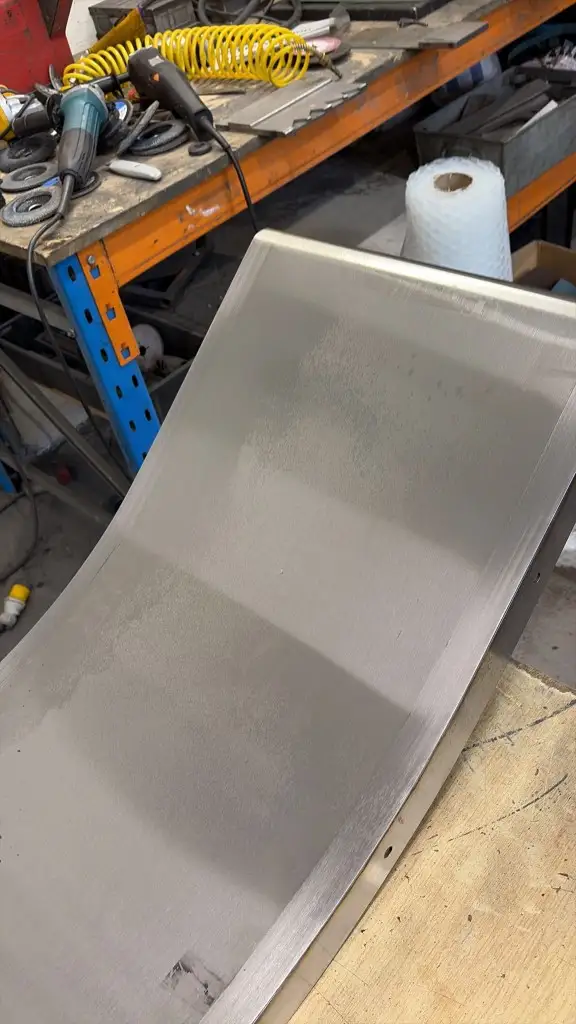 Close-up of a playground slide bed with a brushed finish, rolled profile and flanged edge