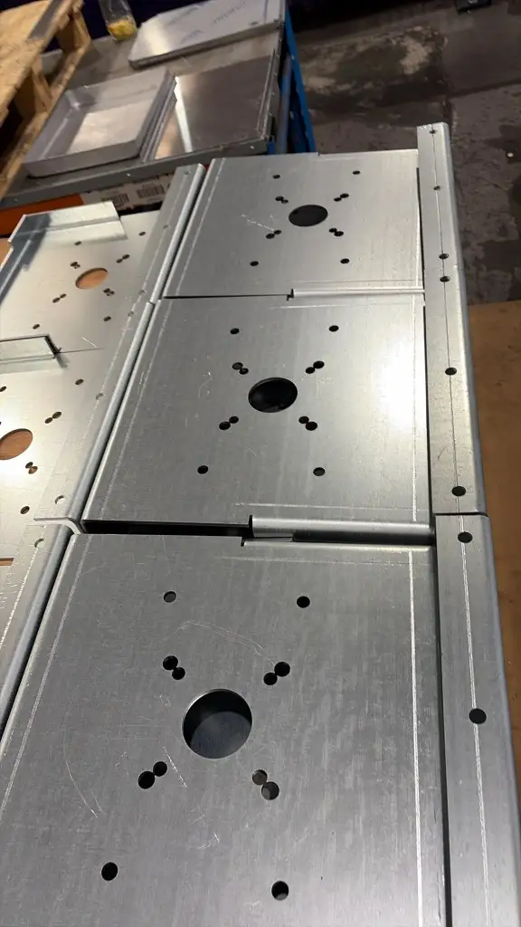 Formed galvanised shutter mounting plates with a central hole, flange edges and a clean nitrogen-cut finish on the bench