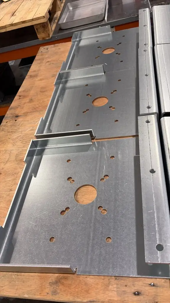 Heavy-duty galvanised mounting plates with laser-cut holes, slots and folded sides laid out on a workshop bench