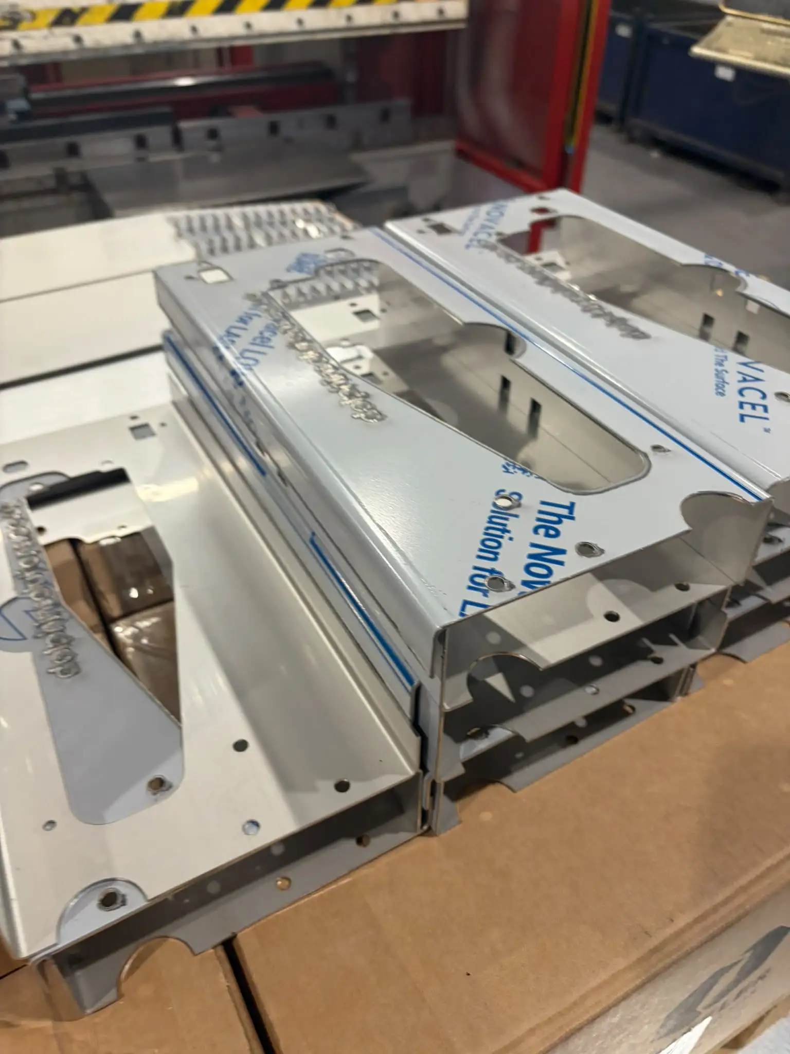 Folded stainless brackets with a large cutout and mounting holes, still in protective film