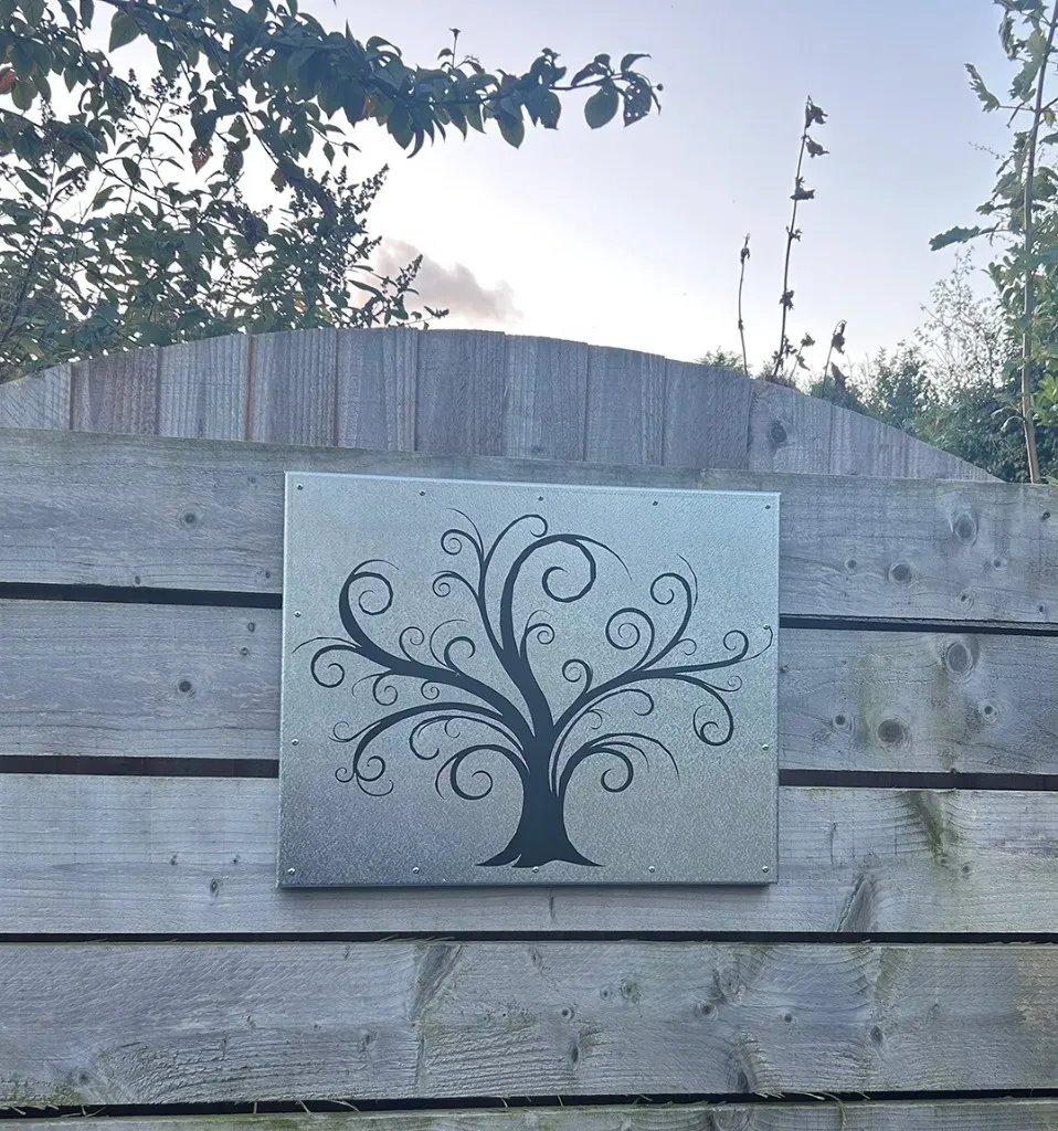 Laser-cut metal garden panel with a swirling tree silhouette mounted on a wooden fence