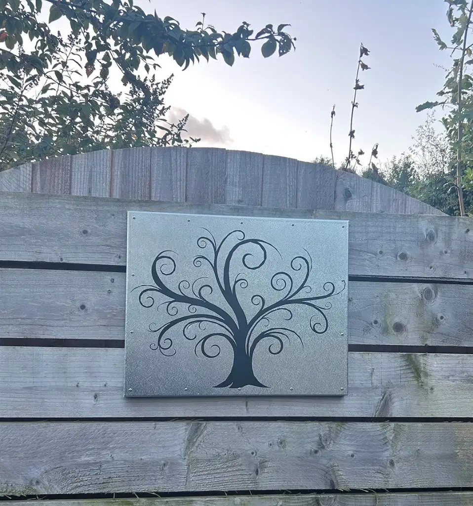 Laser-cut metal garden panel with a swirling tree silhouette mounted on a wooden fence